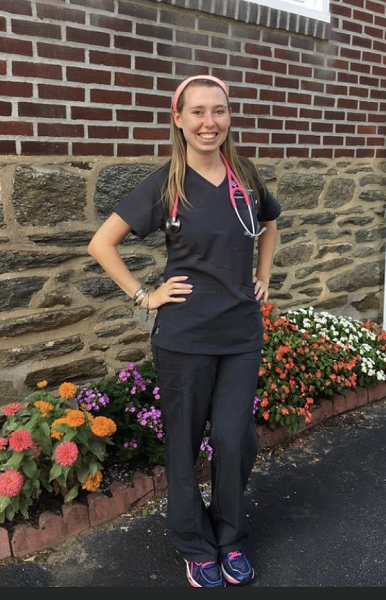 Kelly Gabor in scrubs standing in front of a brick wall and flower beds